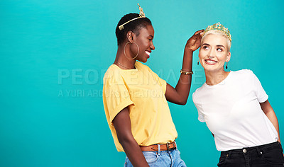 Buy stock photo Studio shot of a young woman putting a crown on her friend against a turquoise background