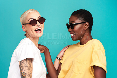Buy stock photo Studio shot of two young women wearing sunglasses against a turquoise background