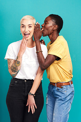 Buy stock photo Studio shot of a young woman whispering in her friend’s ear against a turquoise background