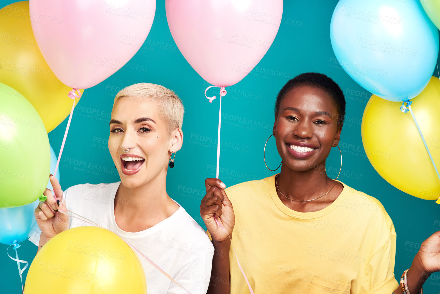 Buy stock photo Studio shot of two young women holding a bunch of colourful balloons against a turquoise background