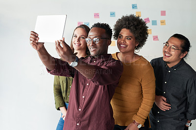 Buy stock photo Shot of a group of young businesspeople taking selfies together with a digital tablet at work