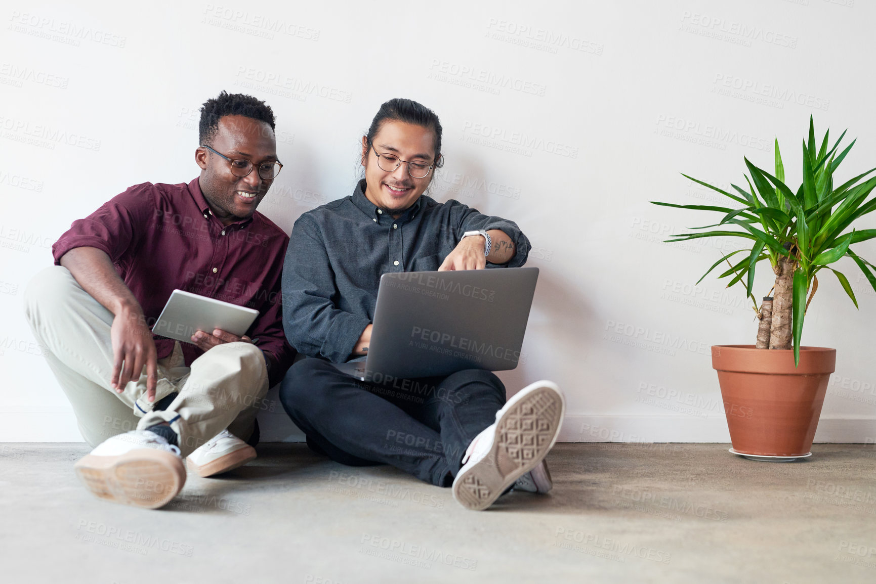 Buy stock photo Full length shot of two young businessmen sitting in the floor and using their digital devices together at work