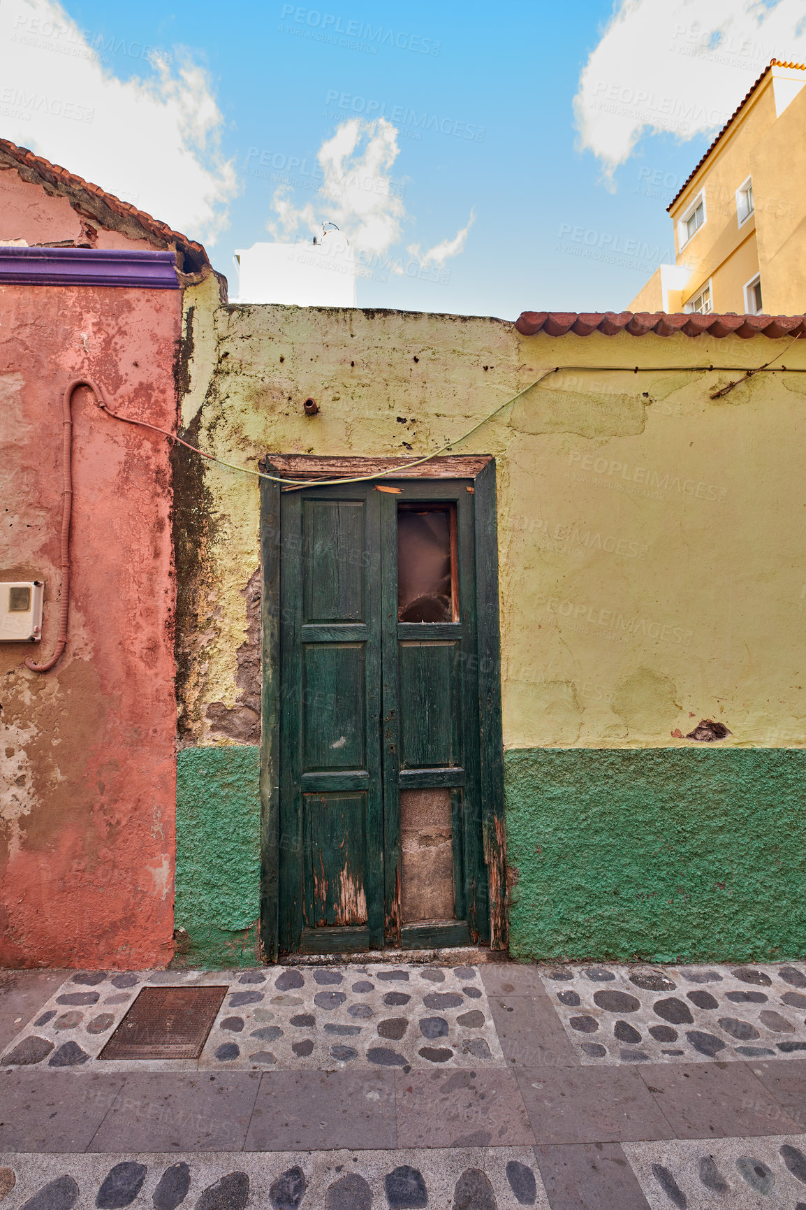 Buy stock photo Old abandoned house or home with a weathered green wall and blue wooden door. Vintage and aged residential building built in a traditional architectural style or design with a blue sky background