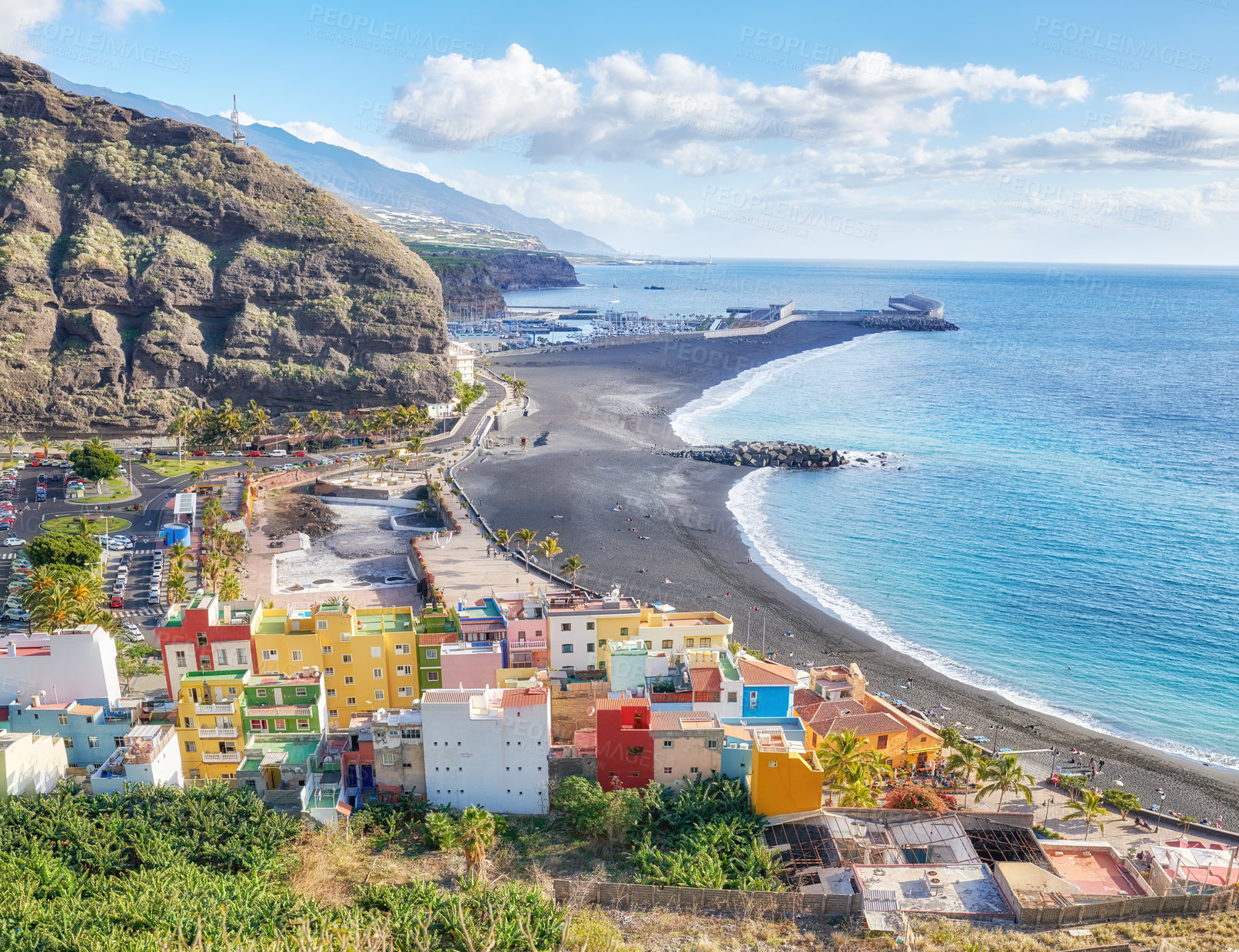 Buy stock photo Landscape view of vibrant residential buildings, sea and ocean, a blue sky with clouds and copy space. Scenic mountain and  black sand beach of coastal city of Puerto de Tazacorte in La Palma, Spain