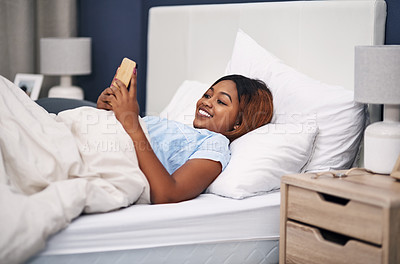 Buy stock photo Cropped shot of an attractive young woman using her cellphone while lying in bed