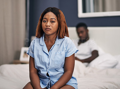 Buy stock photo Cropped portrait of an attractive young woman looking depressed while sitting on the edge of her bed with her husband in the background