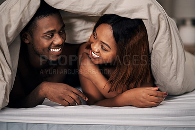 Buy stock photo Cropped shot of an affectionate young couple lying under the covers on their bed at home