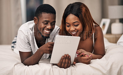 Buy stock photo Cropped shot of an affectionate young couple using a tablet while lying on their bed at home