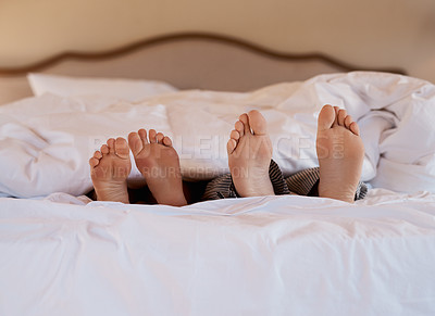 Buy stock photo Shot of an unrecognizable couple's feet poking out under the sheets while lying in bed