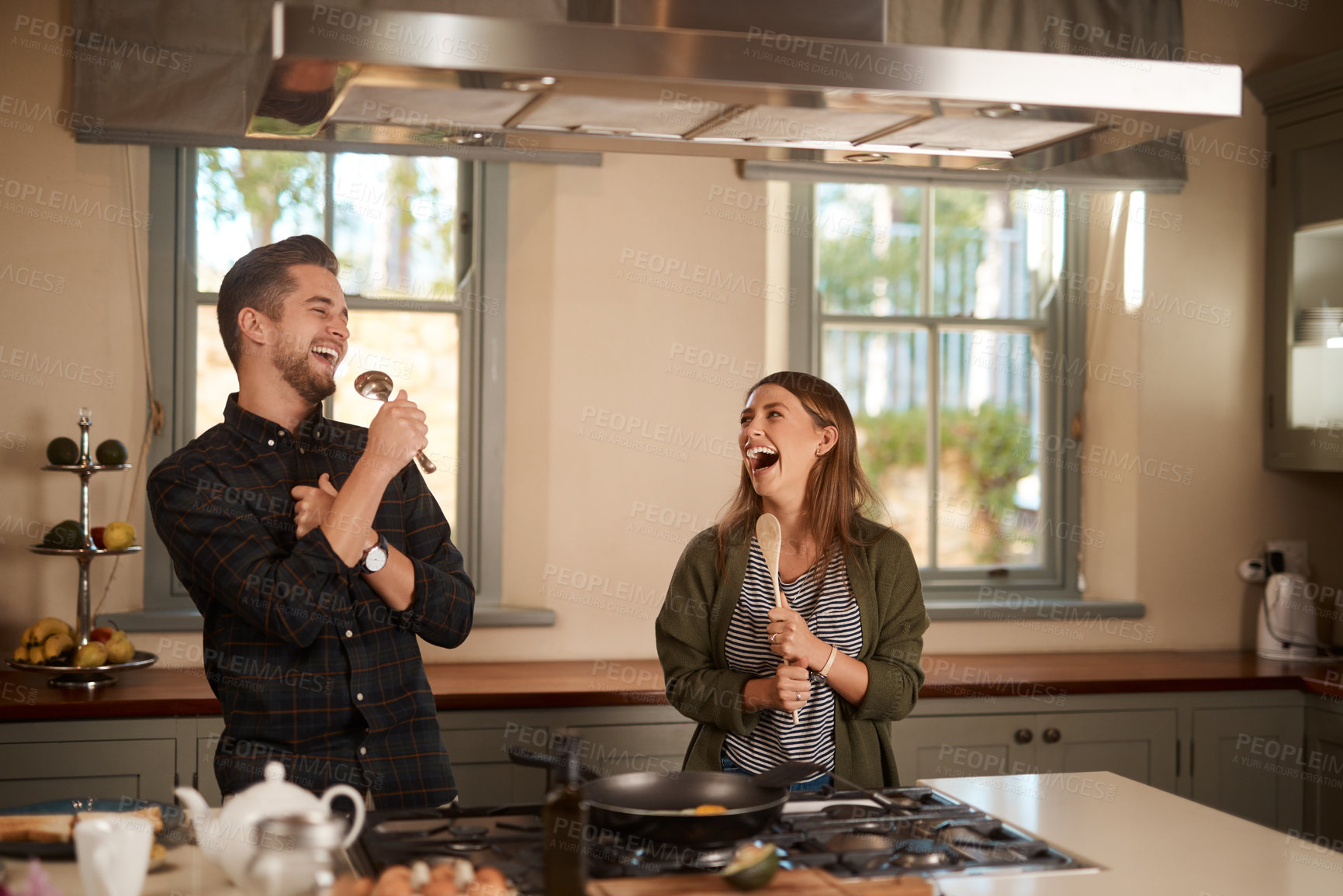 Buy stock photo Food, sing and a silly couple in the kitchen of their home, having fun together while cooking. Karaoke, comic or funny with a man and woman laughing while singing over breakfast in their house