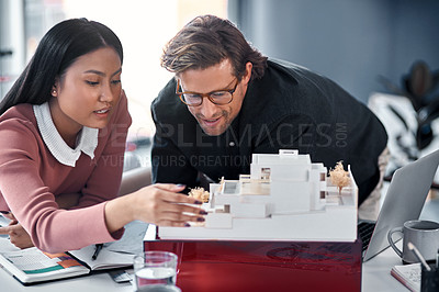Buy stock photo Shot of two young architects working together on a scale model of a modern house in their office