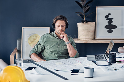 Buy stock photo Shot of a handsome young architect wearing headphones and looking thoughtful while working in his office