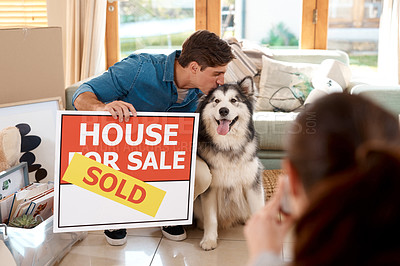 Buy stock photo Shot of a happy young couple and their dog taking photos with a sold sign in their new home