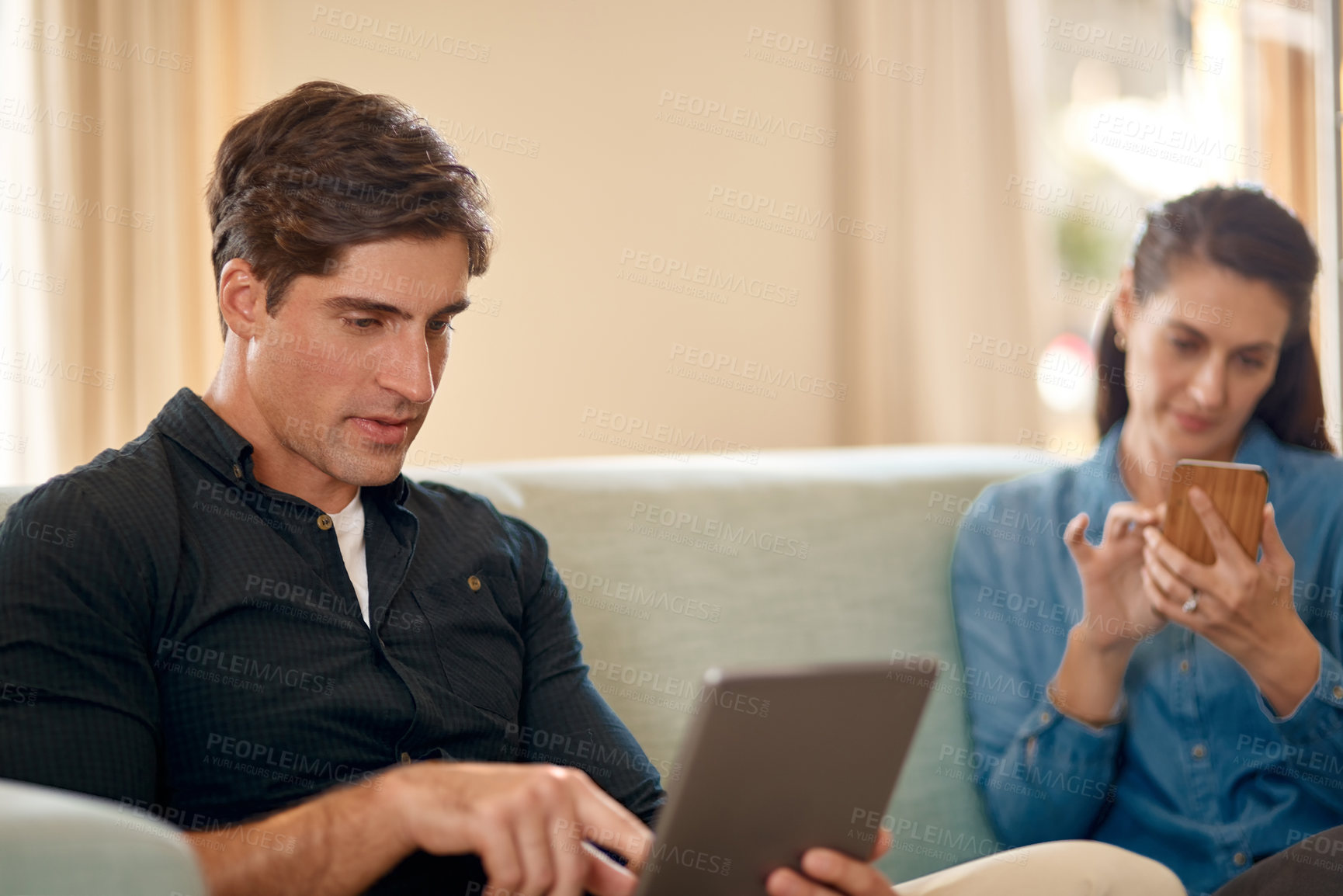 Buy stock photo Cropped shot of a couple using wireless technology while relaxing on the sofa at home