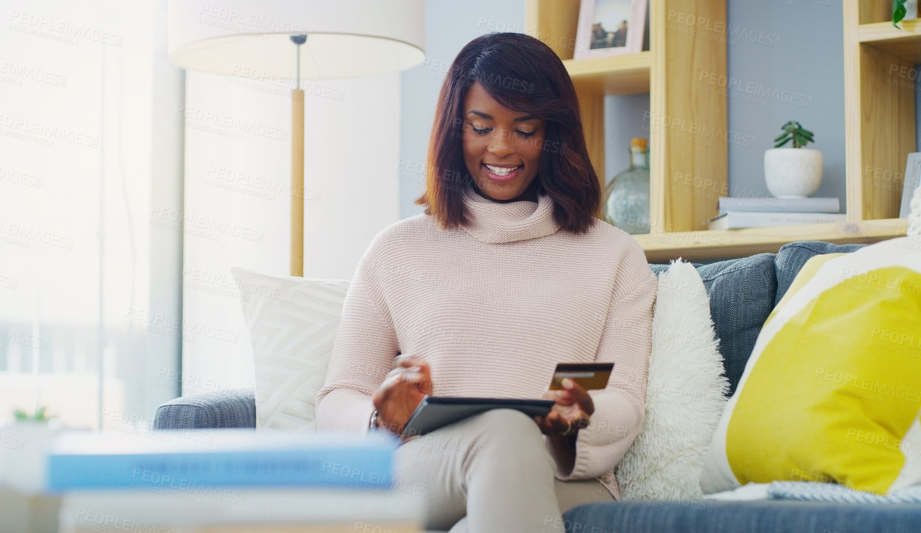 Buy stock photo Shot of an attractive young woman using her digital tablet and credit card while relaxing at home