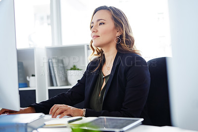 Buy stock photo Shot of a confident young businesswoman using a computer at her desk in a modern office