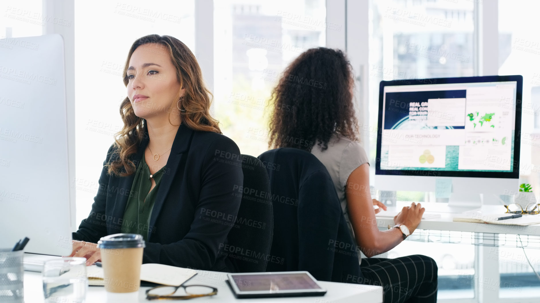 Buy stock photo Shot of two young businesswomen using their computers in a modern office