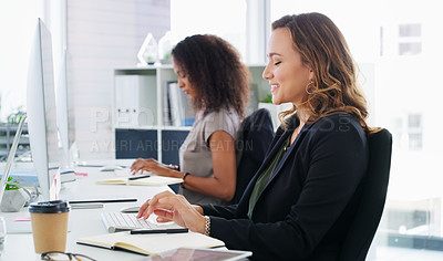 Buy stock photo Shot of two young businesswomen using their computers in a modern office