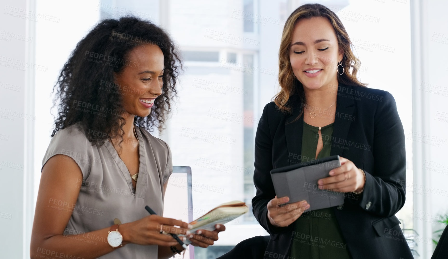 Buy stock photo Shot of two young businesswomen using a digital tablet in a modern office