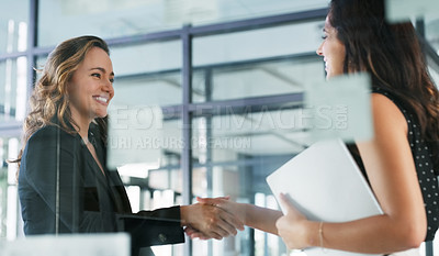 Buy stock photo Cropped shot of two attractive young businesswomen shaking hands while standing in their office