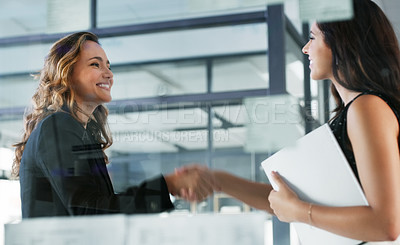 Buy stock photo Low angle shot of two attractive young businesswomen shaking hands while standing in their office