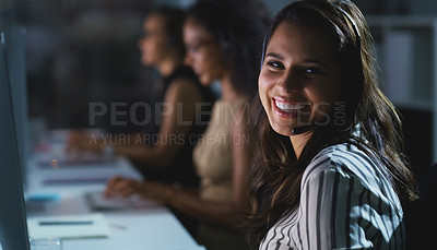 Buy stock photo Cropped portrait of an attractive young female call center agent working late in the office with her colleagues in the background