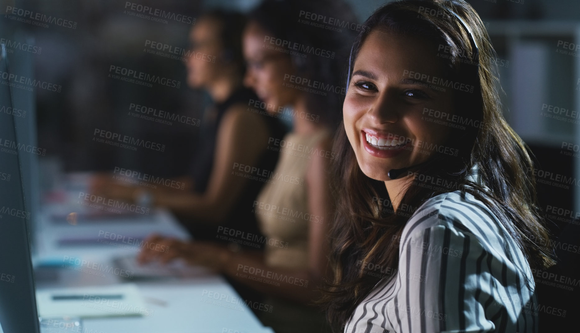 Buy stock photo Cropped portrait of an attractive young female call center agent working late in the office with her colleagues in the background