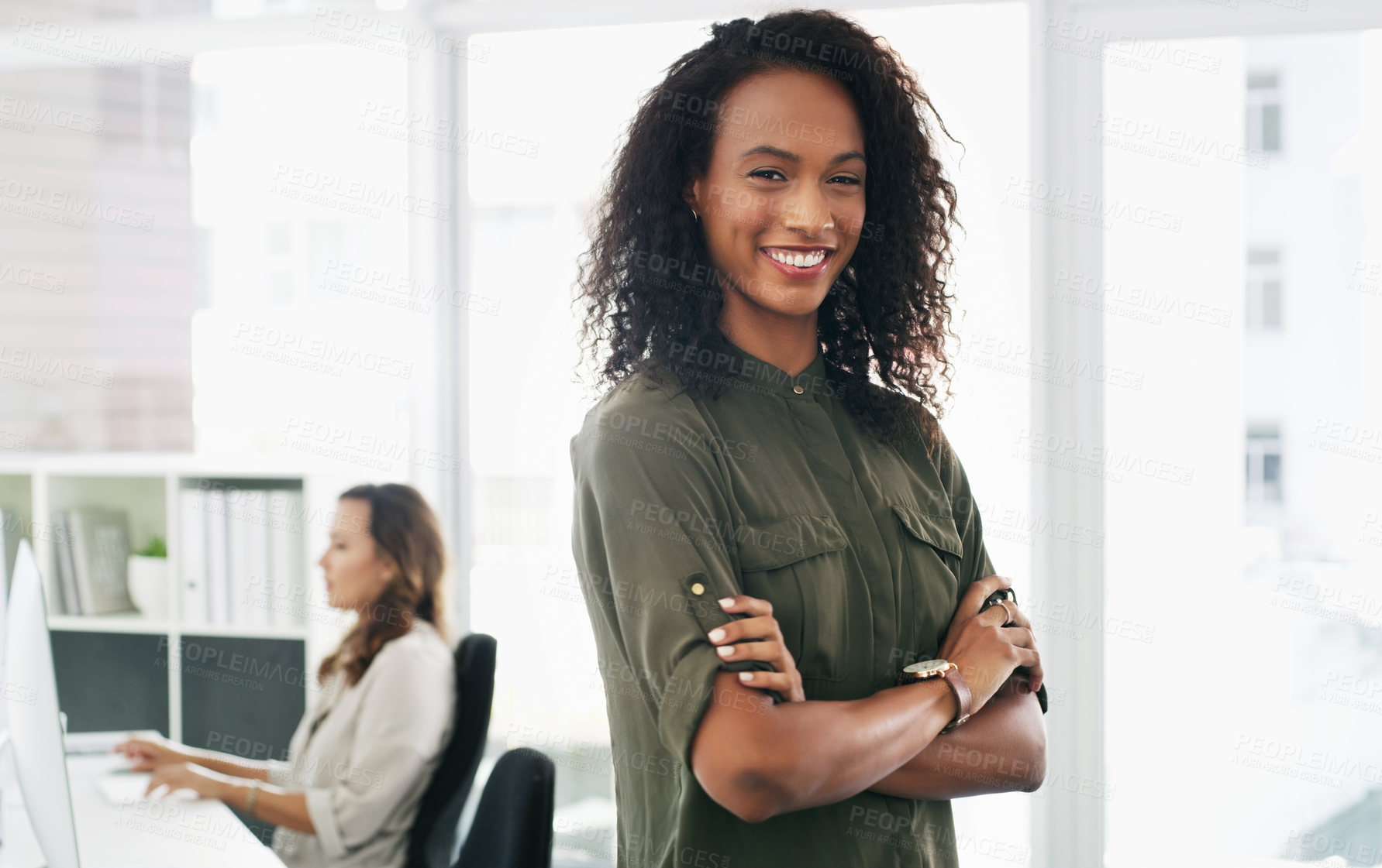 Buy stock photo Portrait of a confident young businesswoman working in a modern office with her colleague in the background