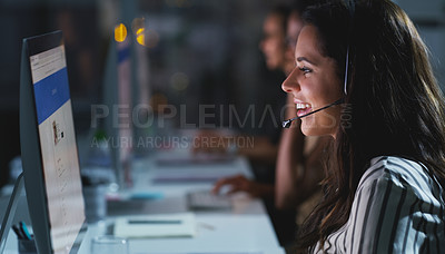Buy stock photo Cropped shot of an attractive young female call center agent working late in the office with her colleagues in the background