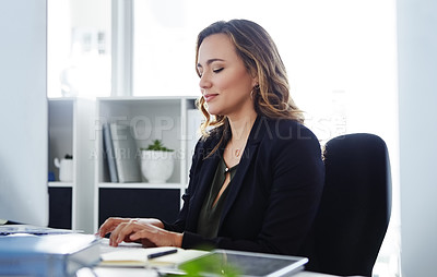 Buy stock photo Shot of a confident young businesswoman using a computer at her desk in a modern office