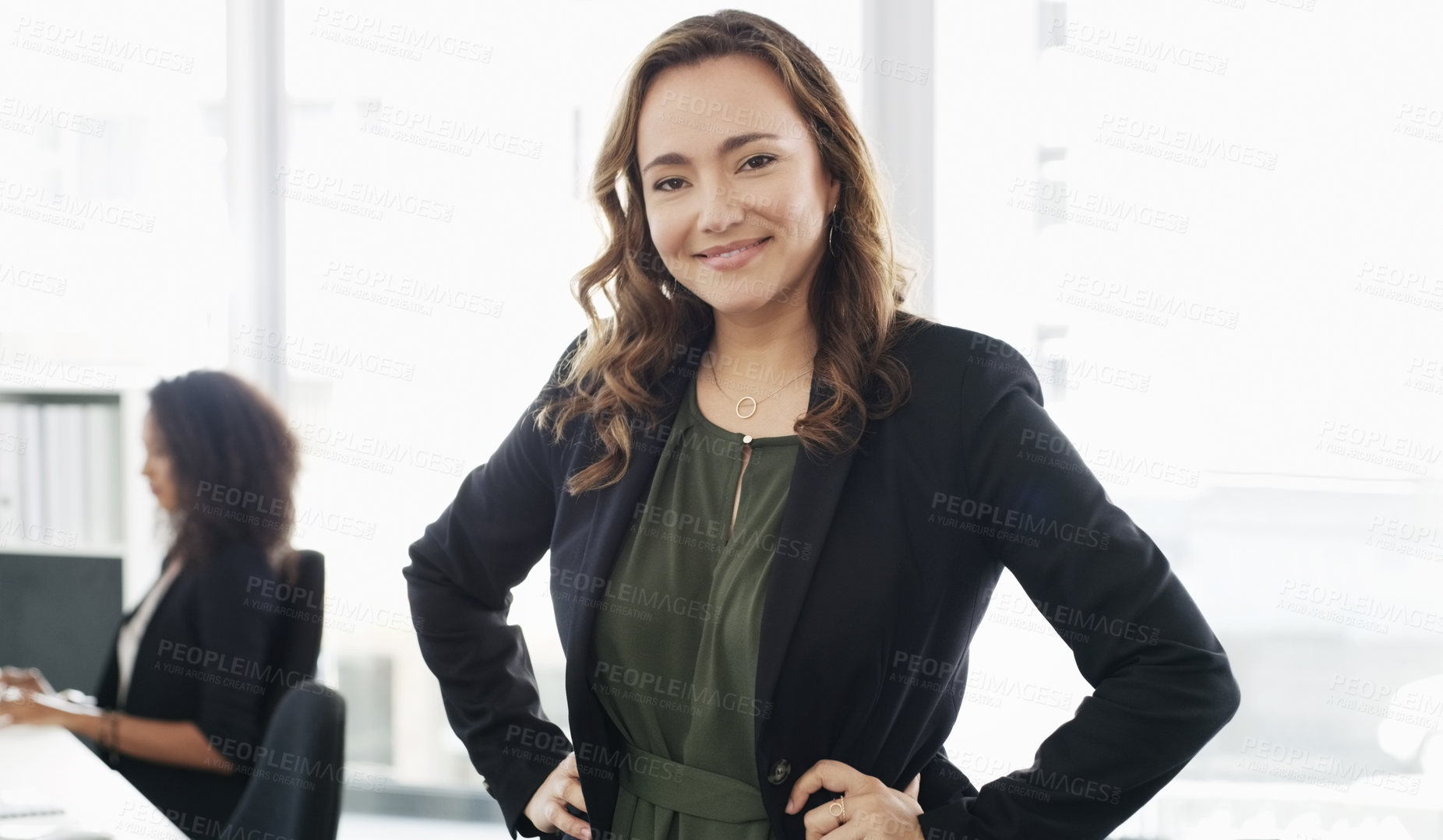 Buy stock photo Portrait of a confident young businesswoman working in a modern office with her colleague in the background