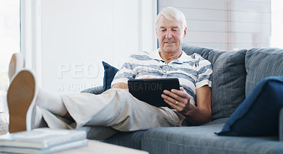 Buy stock photo Shot of a senior man using a digital tablet on the sofa at home