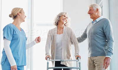 Buy stock photo Shot of a senior woman using a walker with the assistance of her husband and young nurse