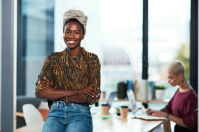 Buy stock photo Cropped portrait of an attractive young businesswoman sitting on the desk in her office while her colleague works behind her