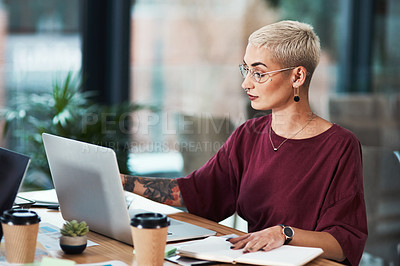 Buy stock photo Cropped shot of an attractive young businesswoman sitting alone in her office and using a laptop while reading her notes