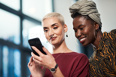 Buy stock photo Cropped shot of two attractive young business colleagues standing in the office together and using a cellphone