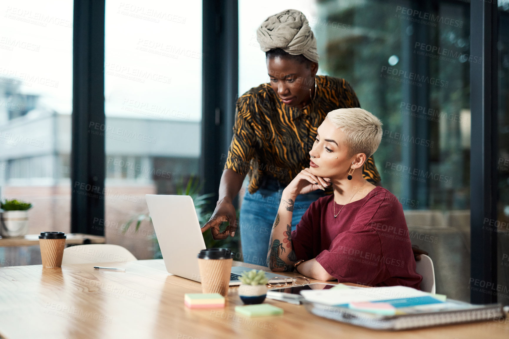 Buy stock photo Cropped shot of two attractive young business colleagues working on a laptop together in the office