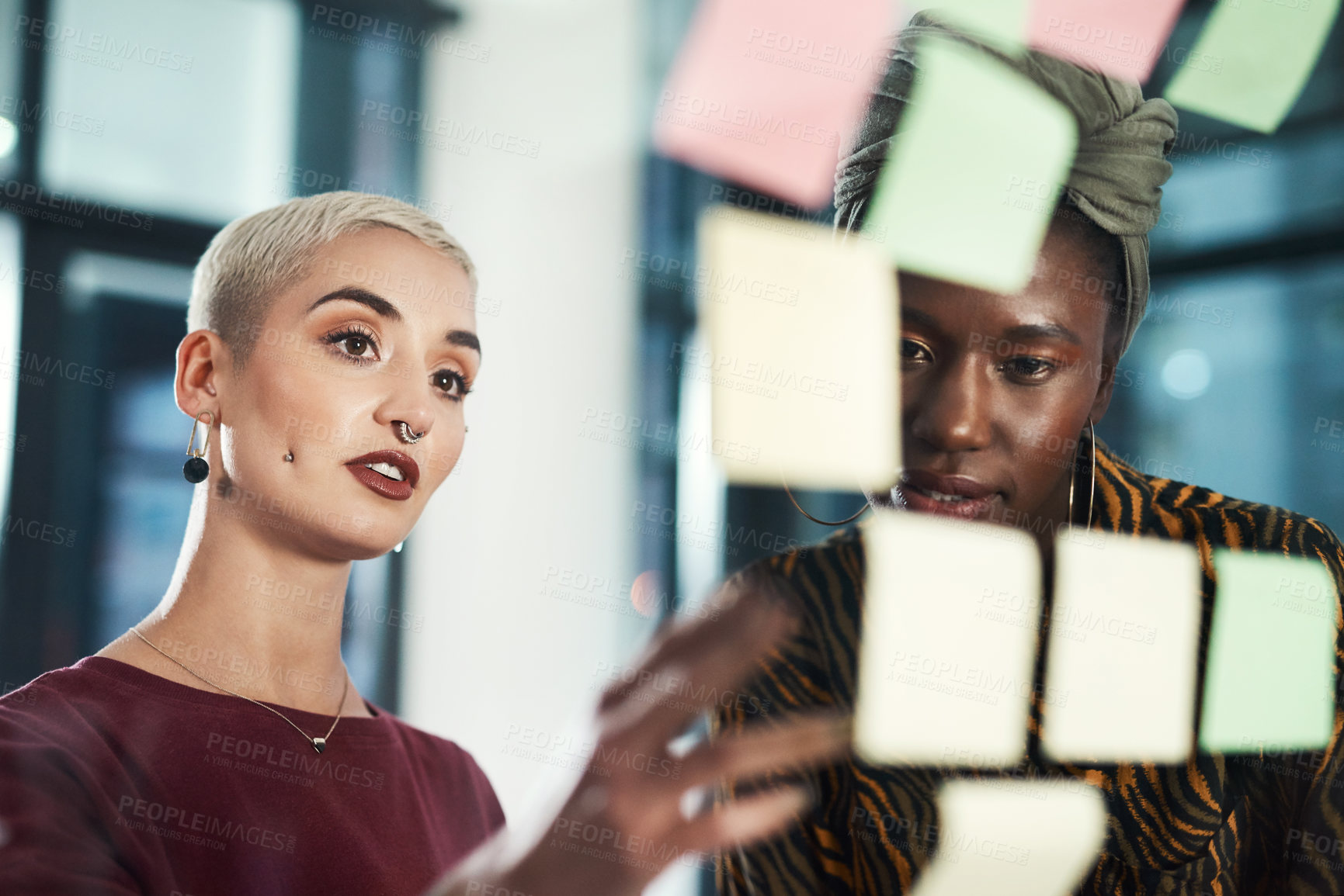Buy stock photo Cropped shot of two attractive young businesswomen standing together in the office and making notes on post-its