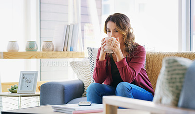 Buy stock photo Cropped shot of an attractive young woman sitting on her living room sofa and drinking a cup of coffee