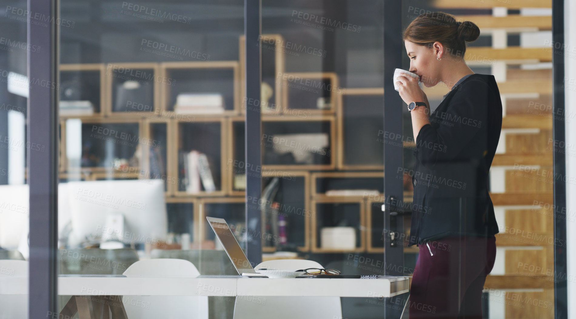 Buy stock photo Cropped shot of an attractive young businesswoman standing alone in her office and drinking a cup of coffee