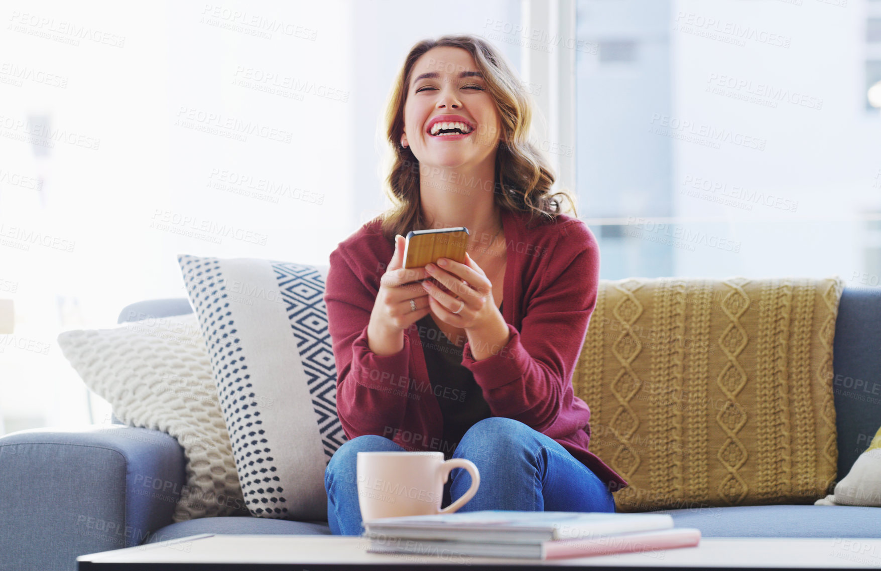 Buy stock photo Cropped shot of an attractive young woman sitting alone on the sofa in her living room and using her cellphone