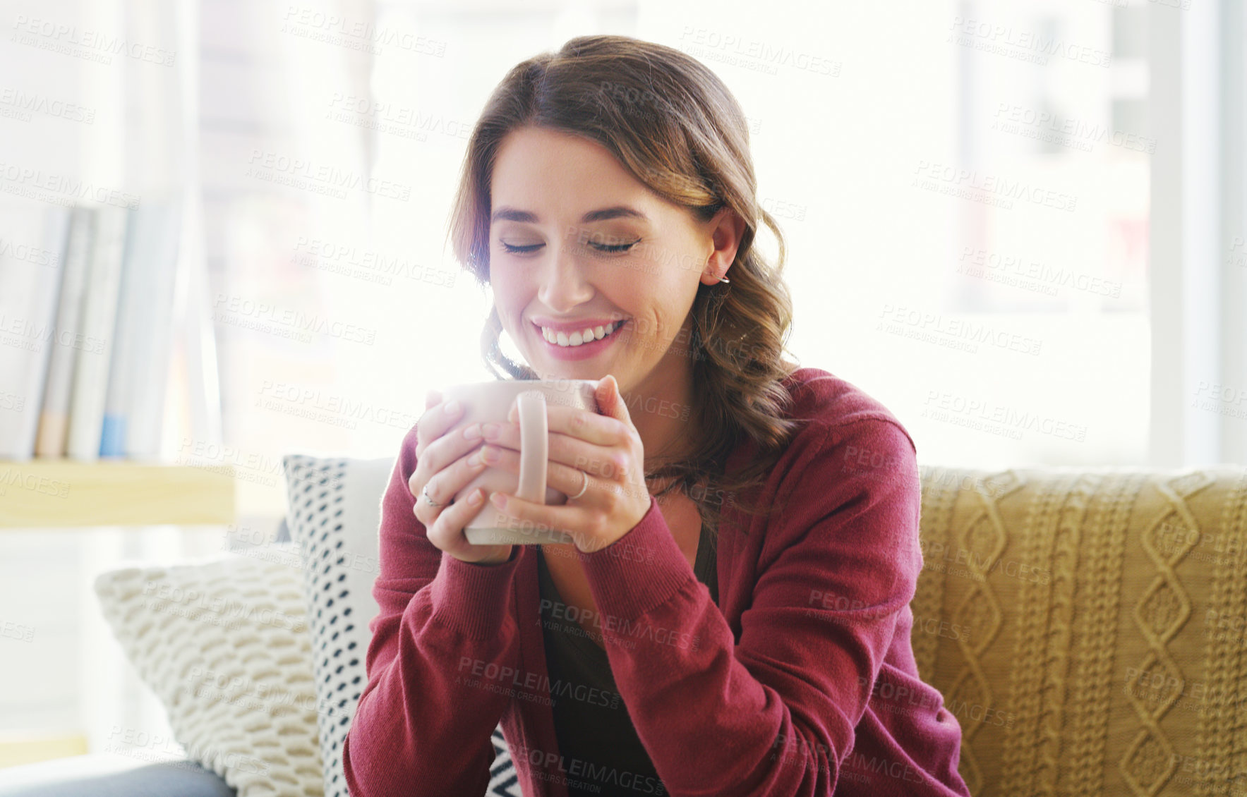 Buy stock photo Cropped shot of an attractive young woman sitting on her living room couch and enjoying a cup of coffee