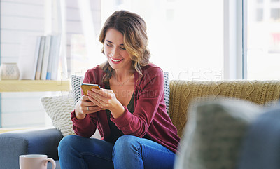 Buy stock photo Cropped shot of an attractive young woman sitting alone on the sofa in her living room and using her cellphone