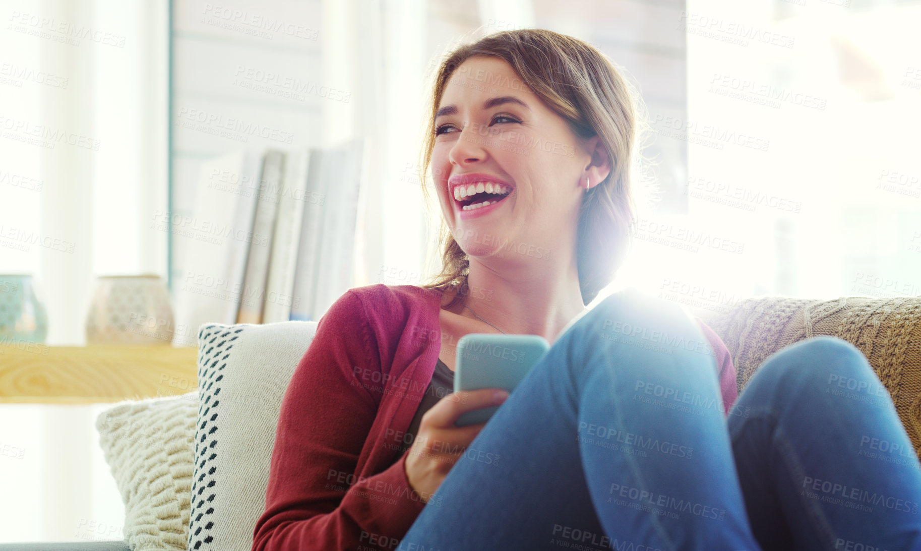 Buy stock photo Cropped shot of an attractive young woman sitting on her sofa alone and laughing while using her cellphone