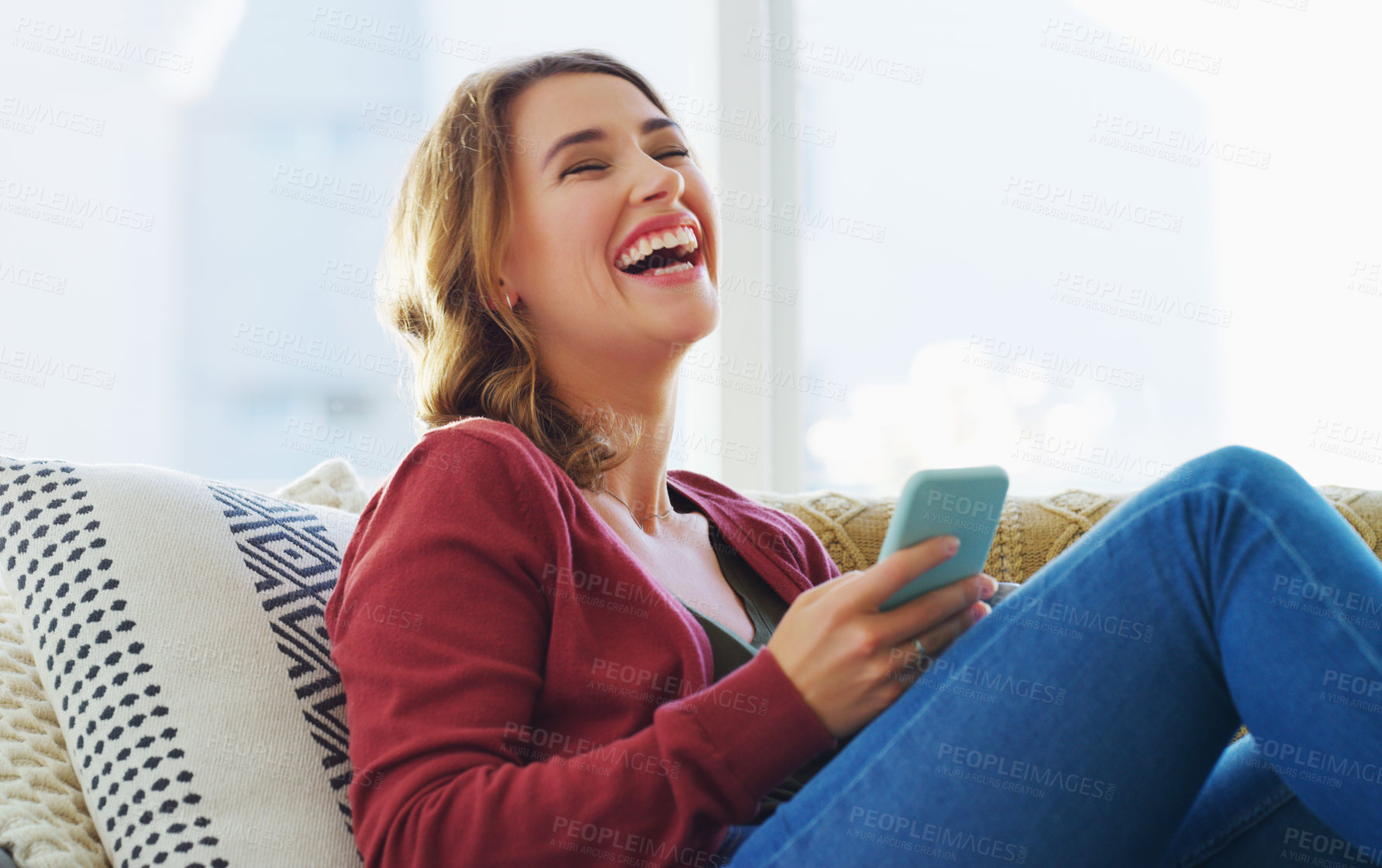 Buy stock photo Cropped shot of an attractive young woman sitting on her sofa alone and laughing while using her cellphone