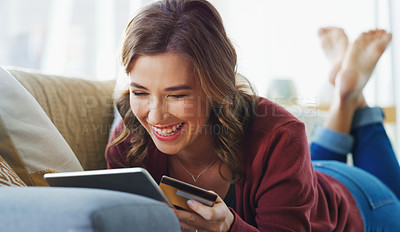 Buy stock photo Cropped shot of an attractive young woman lying down on her sofa and using a tablet for online shopping
