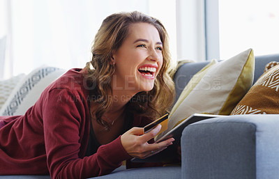 Buy stock photo Cropped shot of an attractive young woman lying down on her sofa and using a tablet for online shopping
