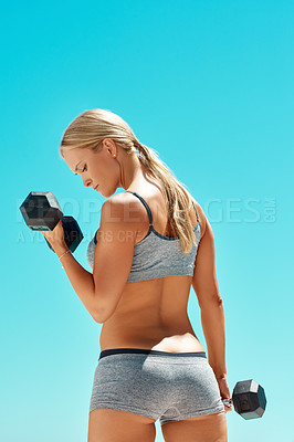 Buy stock photo Rearview shot of an attractive young woman exercising with dumbbells outside