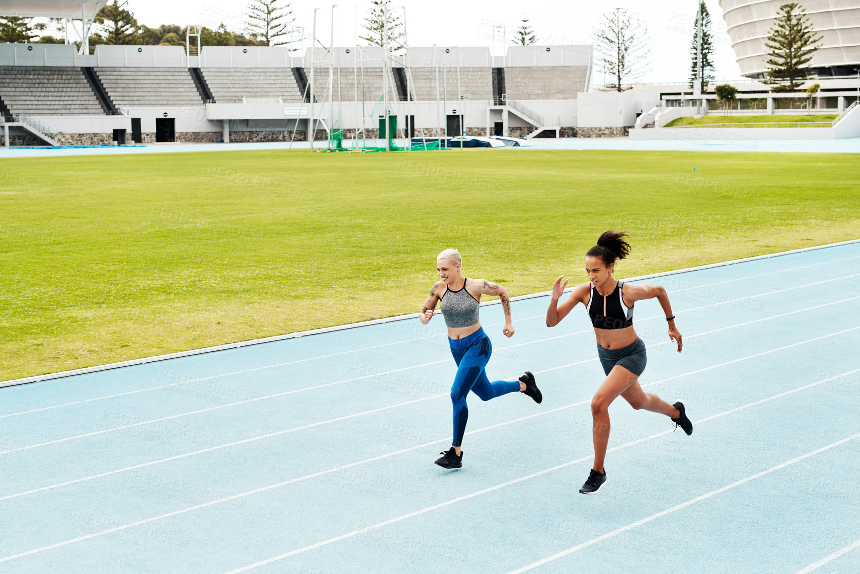 Buy stock photo Full length shot of two attractive young athletes running a track field together during an outdoor workout session