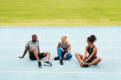 Buy stock photo Full length shot of a diverse group of athletes sitting together after a team training session on a running track